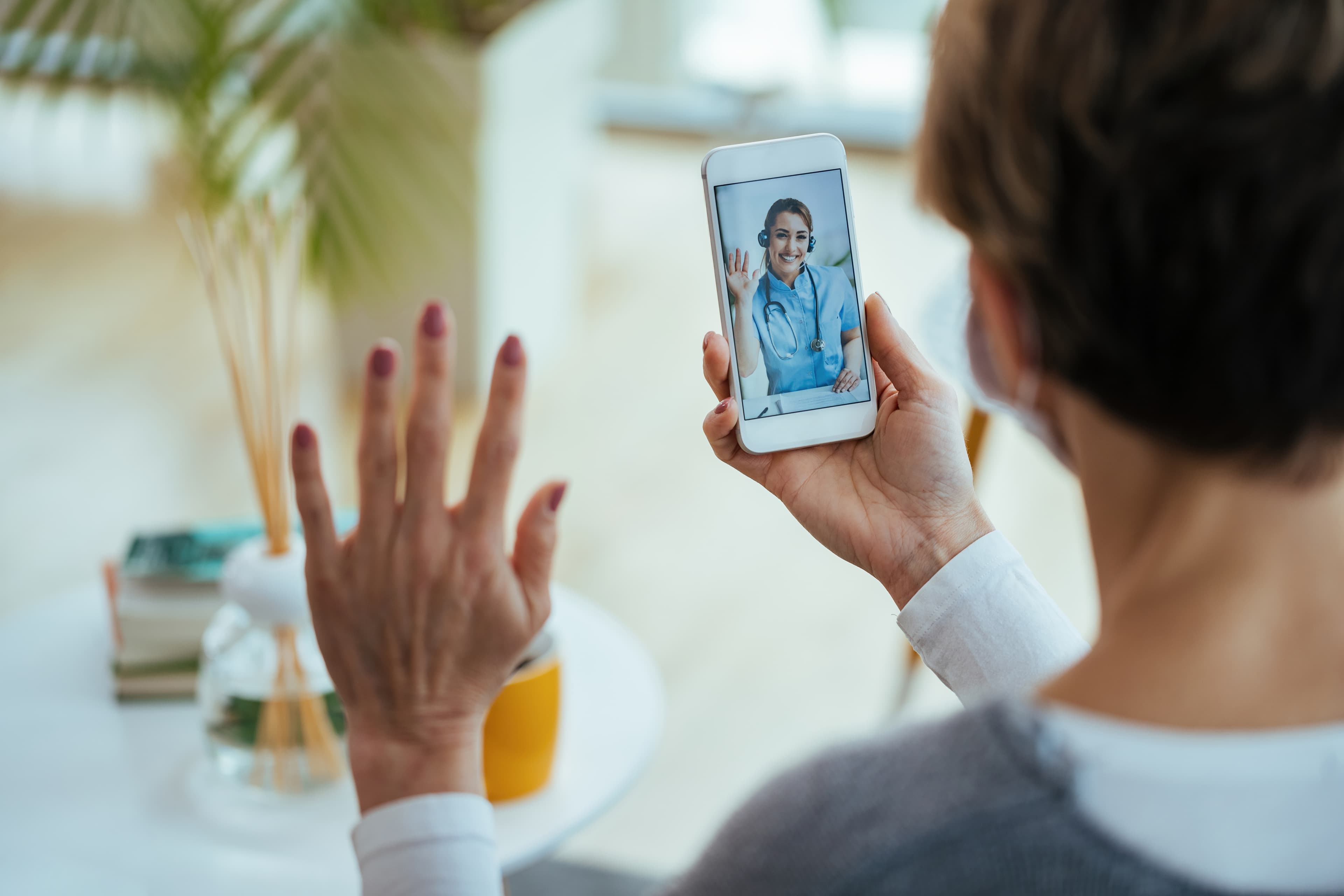 An older woman on a video call with her doctor on a smartphone, with the doctor visible on the screen.